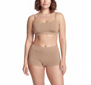 A woman modeling a matching beige two-piece lingerie set consisting of a wireless bralette and high-waisted briefs, shot against a solid white background.