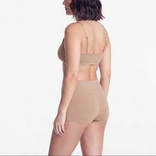 A woman shown from the back wearing a matching beige bralette and high-waisted brief set against a plain white studio background.