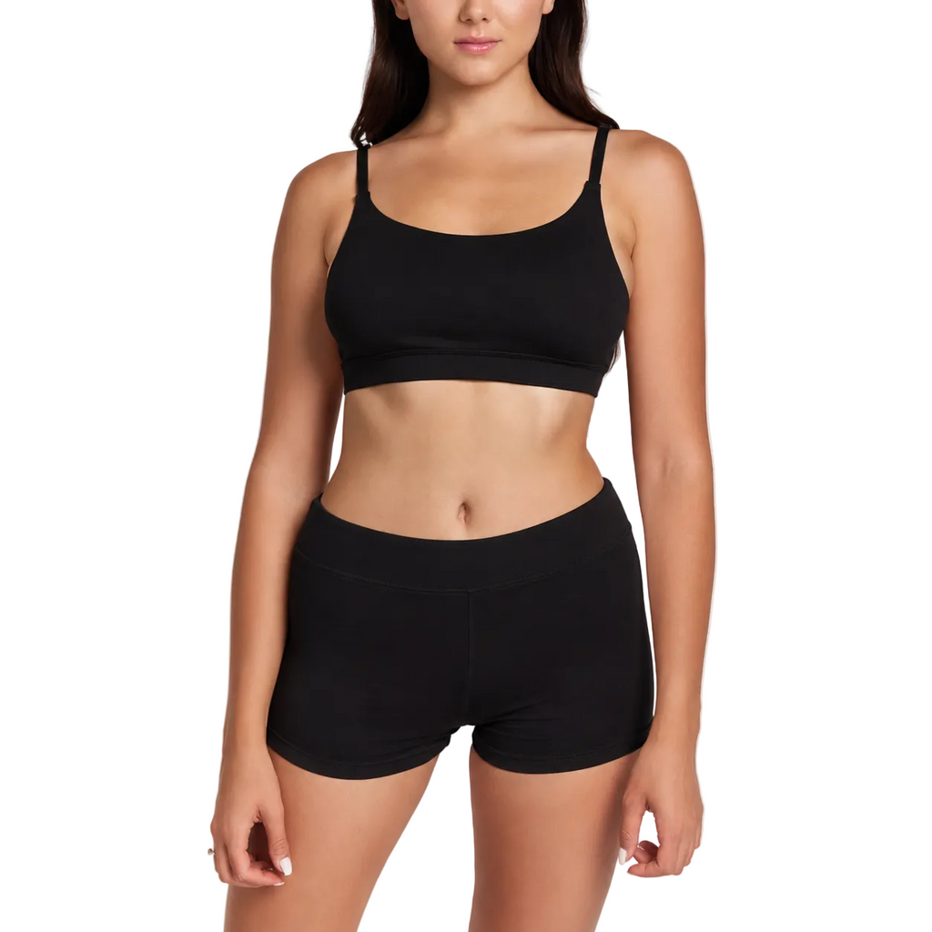 A woman modeling a black two-piece activewear set consisting of a scoop-neck sports bra and matching high-waisted shorts, shot against a plain light gray studio background.